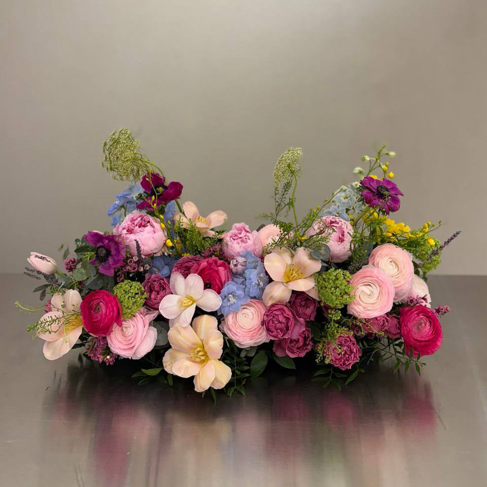  Low floral centerpiece with pink peonies, ranunculus, roses, blue delphinium, anemone, and greenery, approx.