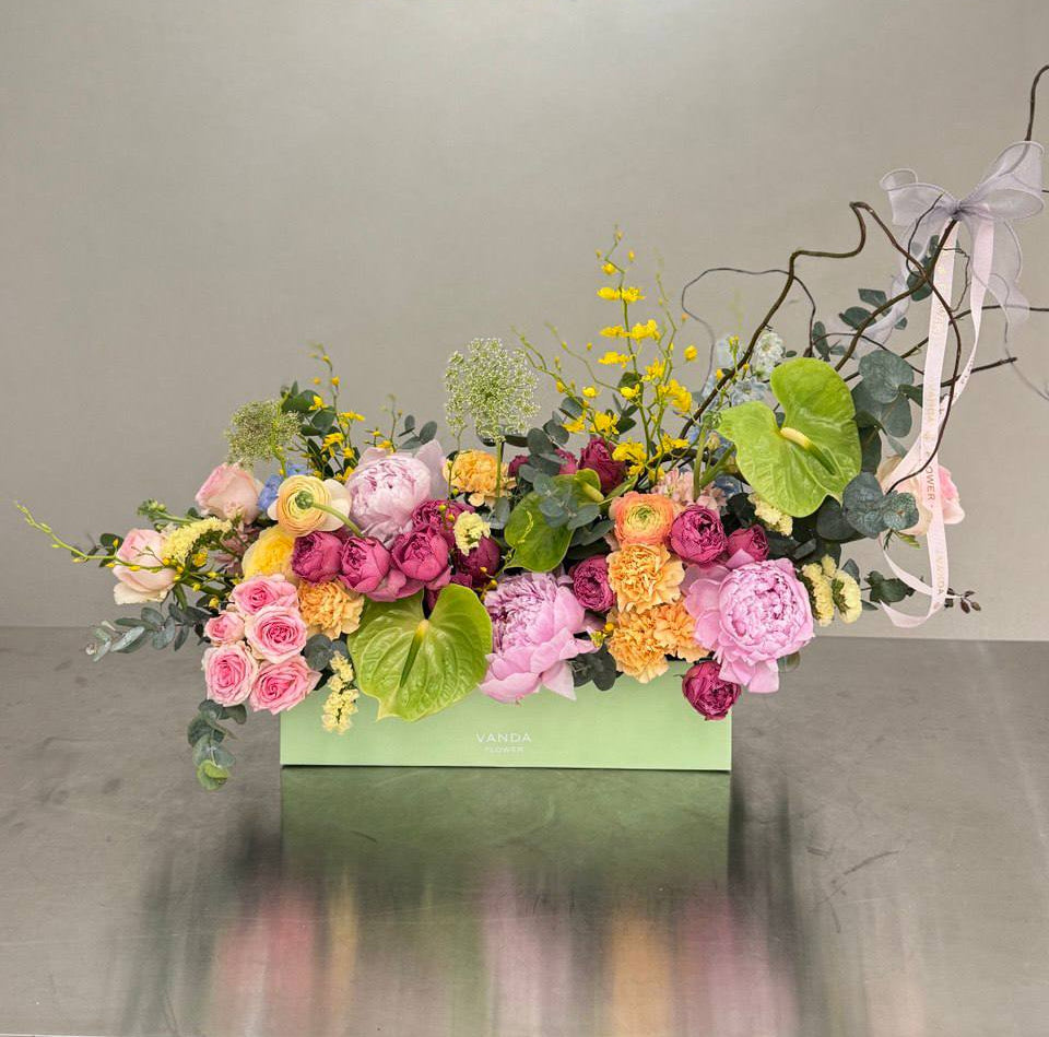 Small rectangular flower box with pink peonies, roses, ranunculus, yellow oncidium, green anthurium, eucalyptus, and curly willow
