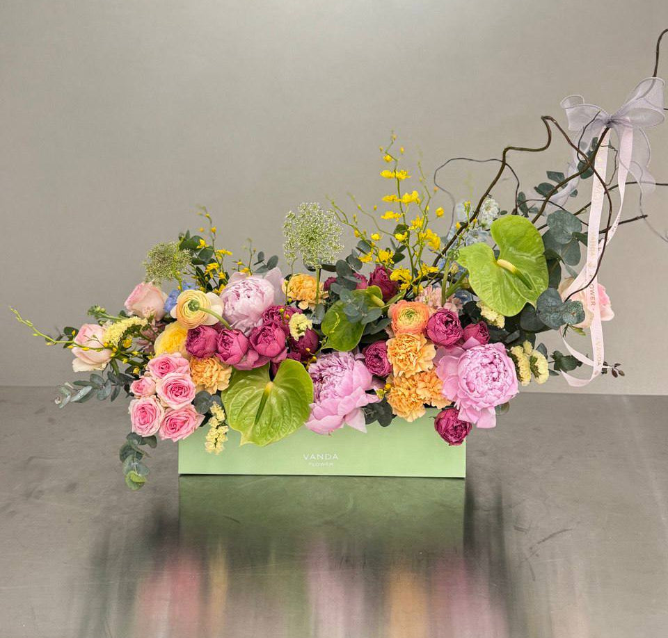 Large rectangular flower box with pink peonies, roses, ranunculus, yellow oncidium, green anthurium, eucalyptus, and curly willow