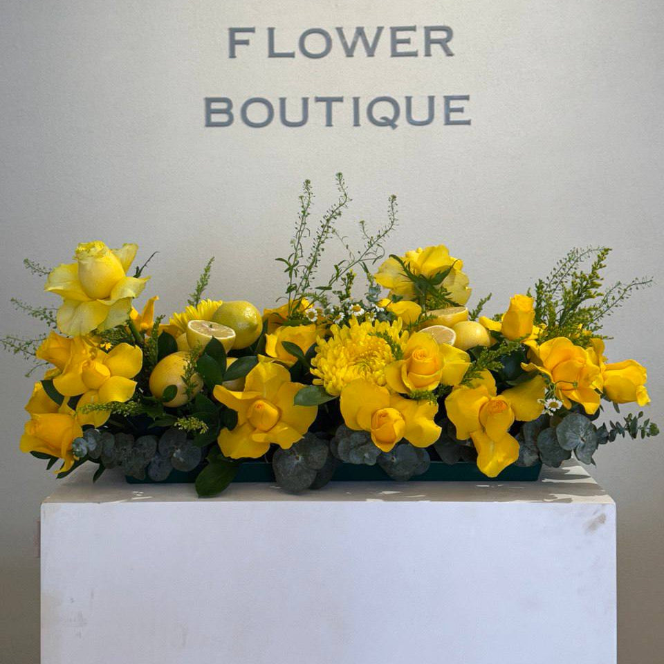  Long low yellow floral centerpiece with roses, cymbidium orchids, chrysanthemums, eucalyptus, solidago, and fresh lemon accents