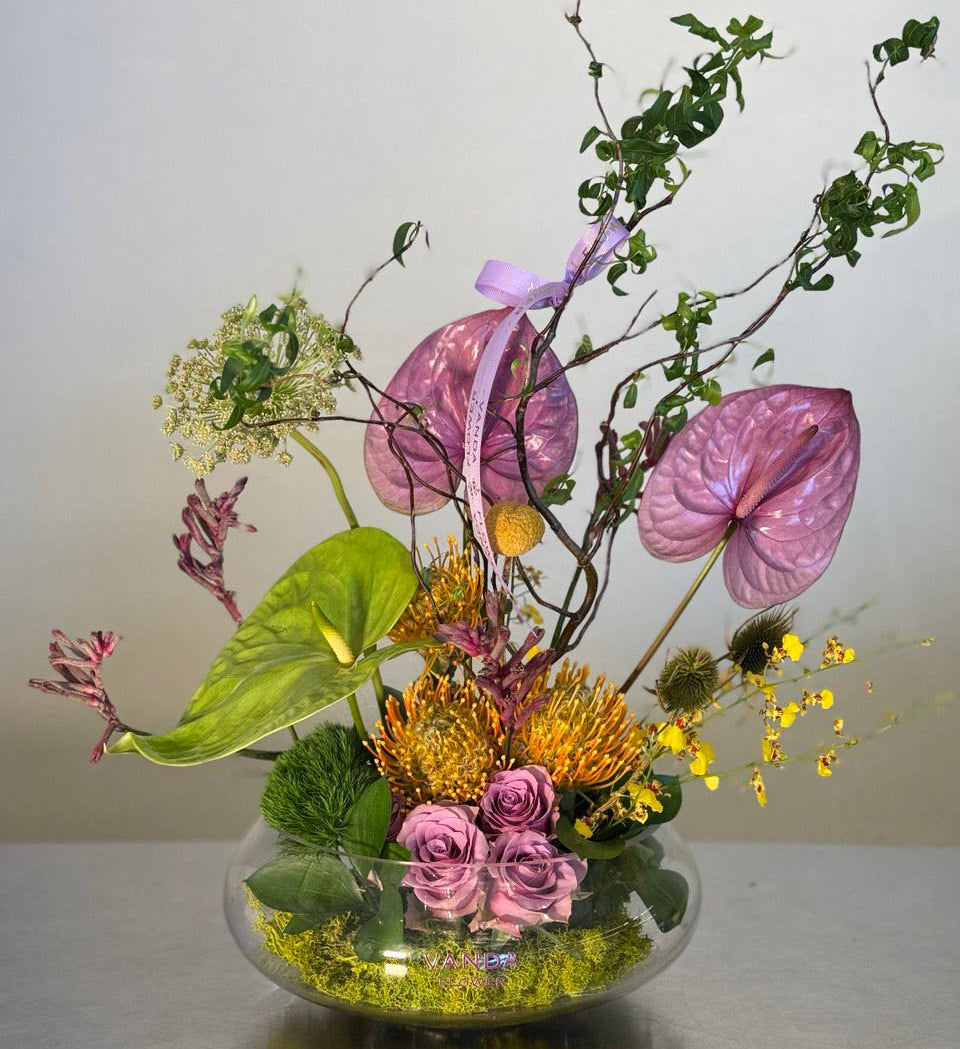 Luxury artistic fresh flower arrangement in a glass bowl with purple anthuriums roses and mixed seasonal flowers