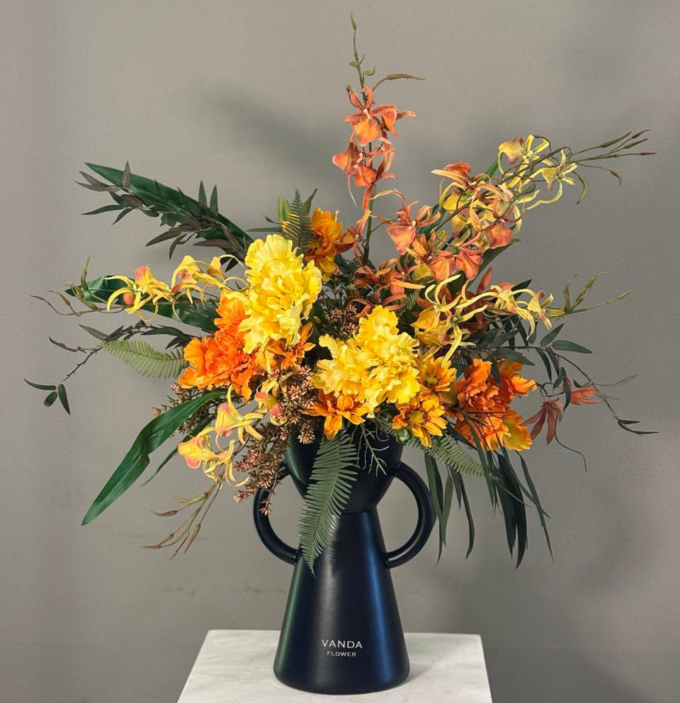 Luxury fresh flower arrangement in sunset yellow and orange tones styled in a black designer vase
