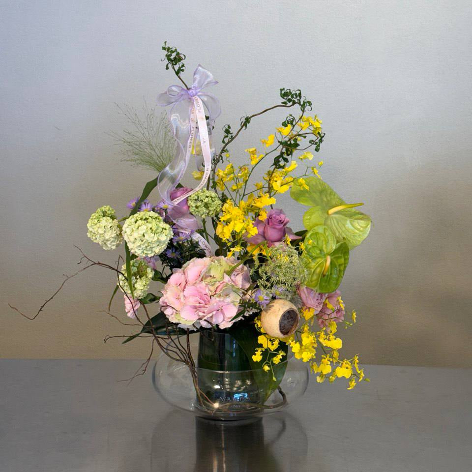 Luxury fresh flower arrangement in pastel tones with yellow accents arranged in a clear glass bowl